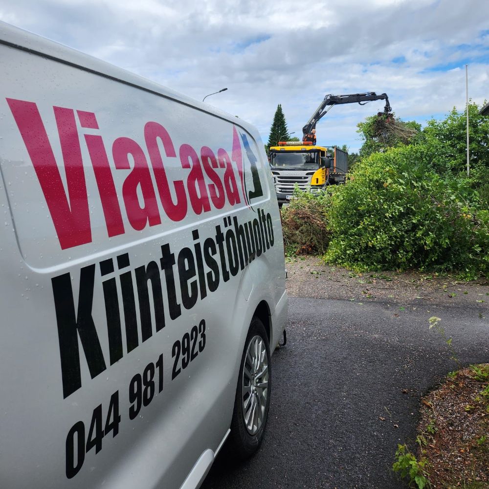ViaCasan viherpalvelu – risunkeruu ja pihatyöt Heinolassa ViaCasan pakettiauto työmaa-alueella, taustalla koura-auto lastaa hakkuujätettä lavalle osana piha-alueen raivausta.